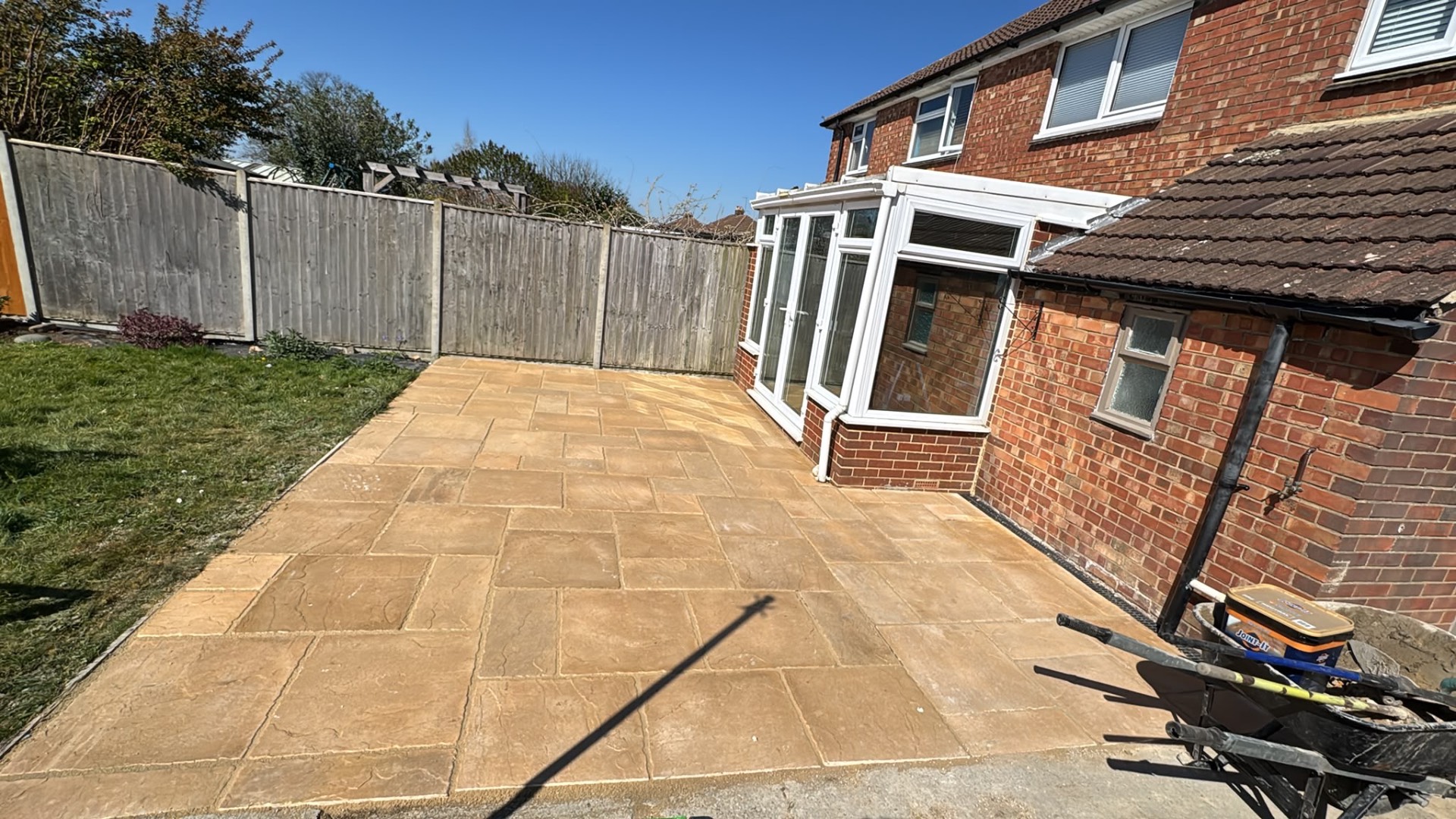 Buff riven slab patio in a rear garden beside a conservatory, jointing compound in progress