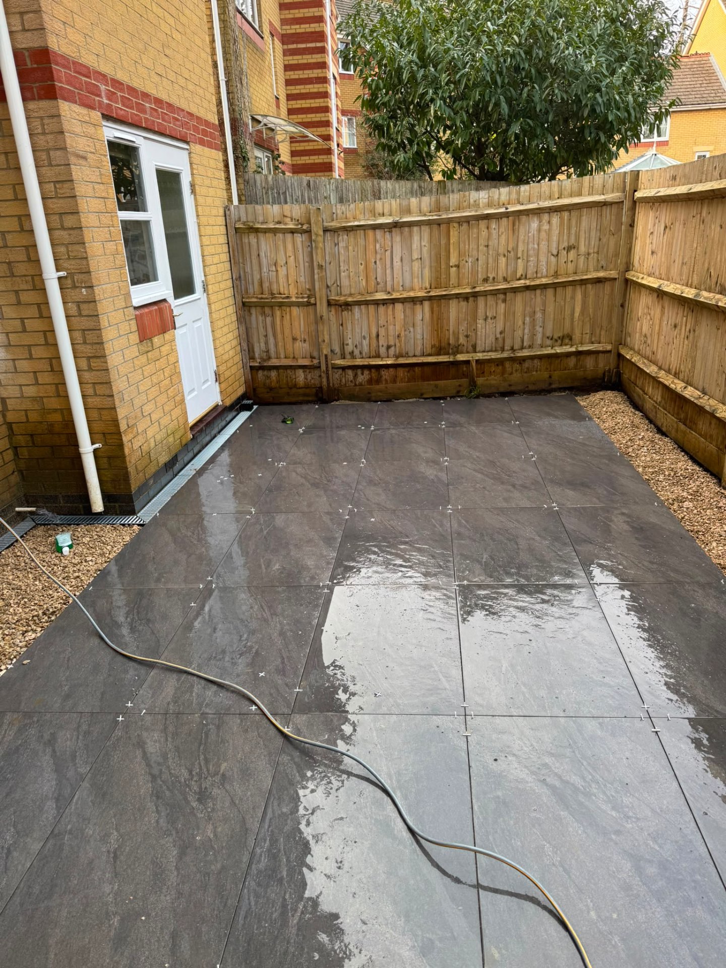 Slate-effect porcelain courtyard in Gloucester with gravel margins against a close-board fence