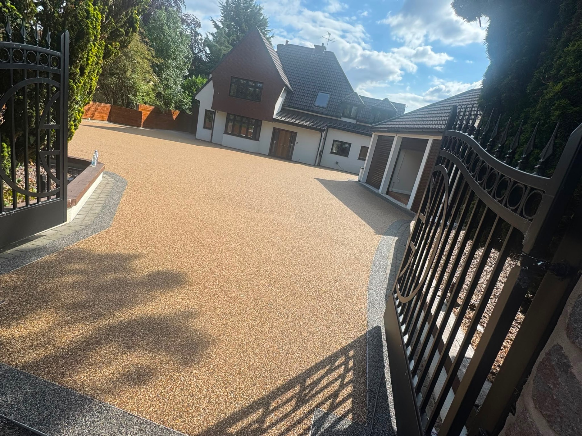 Large gold resin bound gated driveway with block paved border at a detached Gloucester house