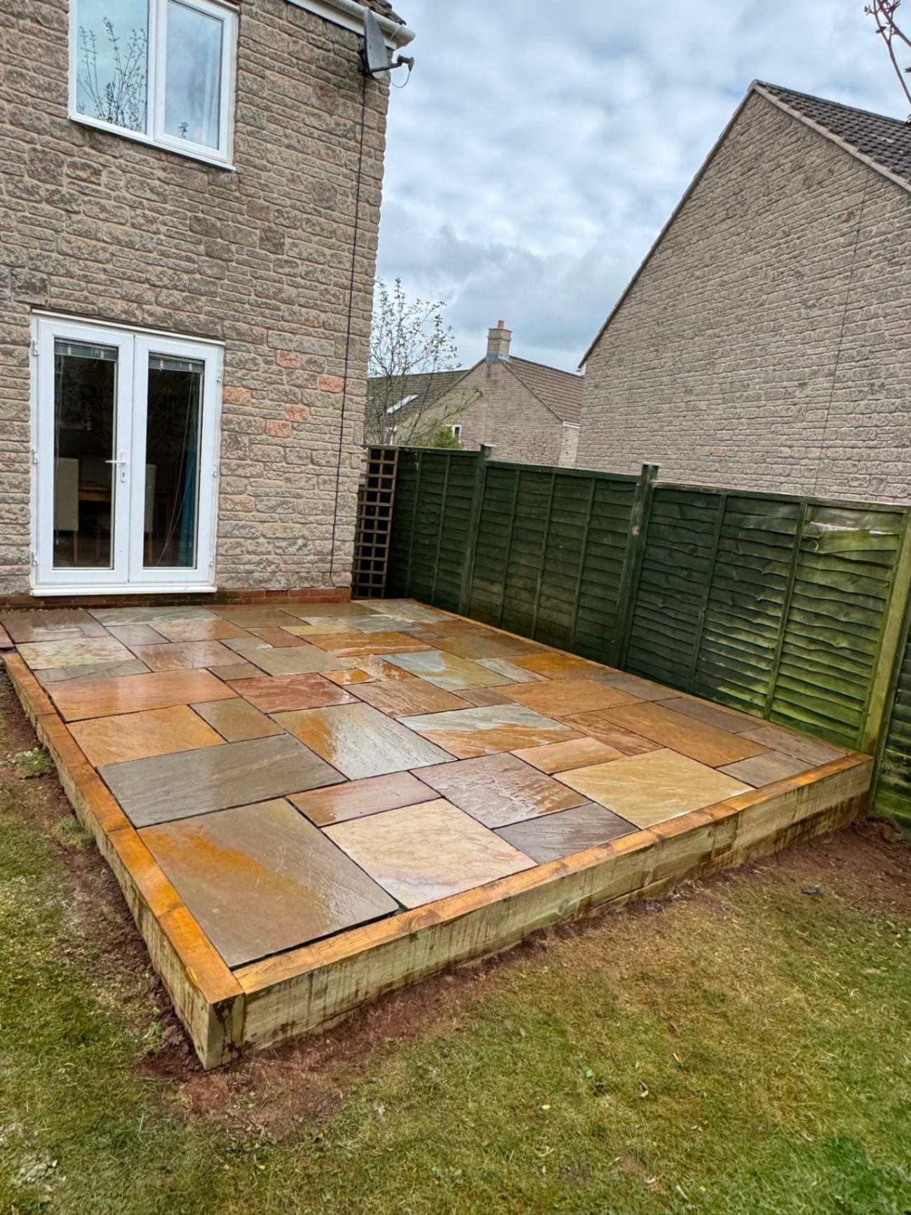 Raised Indian sandstone patio with timber sleeper edging outside French doors in Gloucester