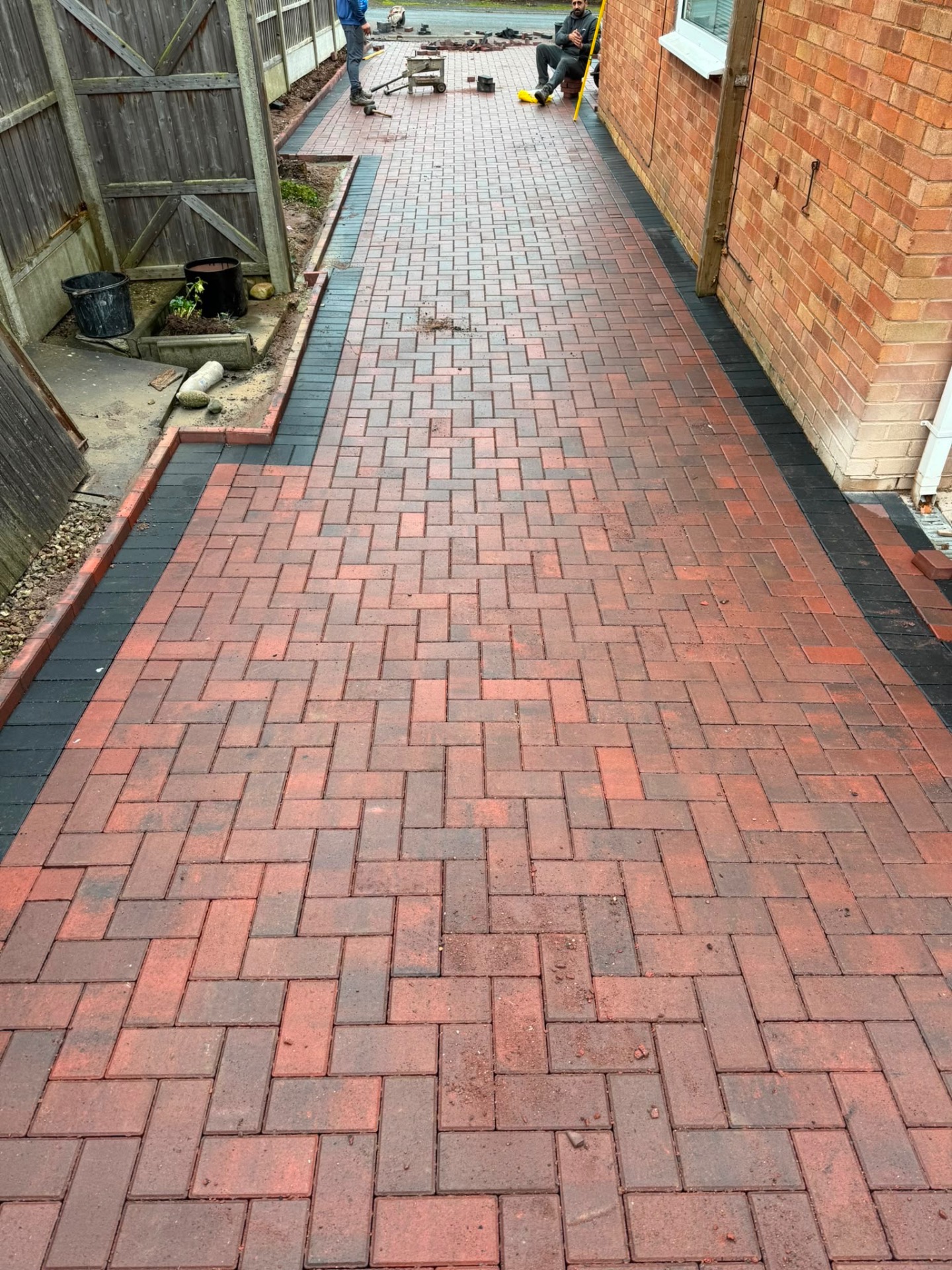 Red brindle block paved side passage under construction in Gloucester, with charcoal border course and red brick kerb