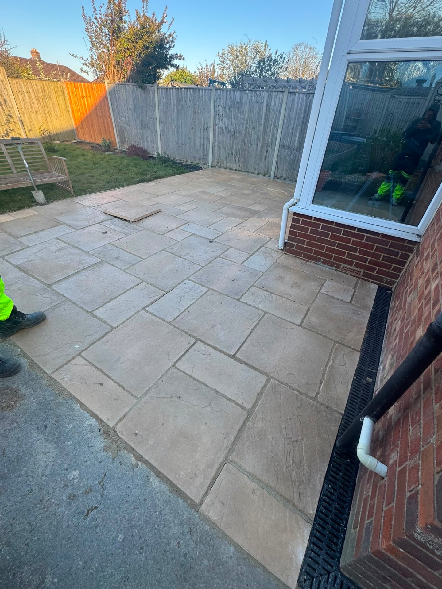 Grey riven slab patio laid around a conservatory with a black channel drain along the brickwork