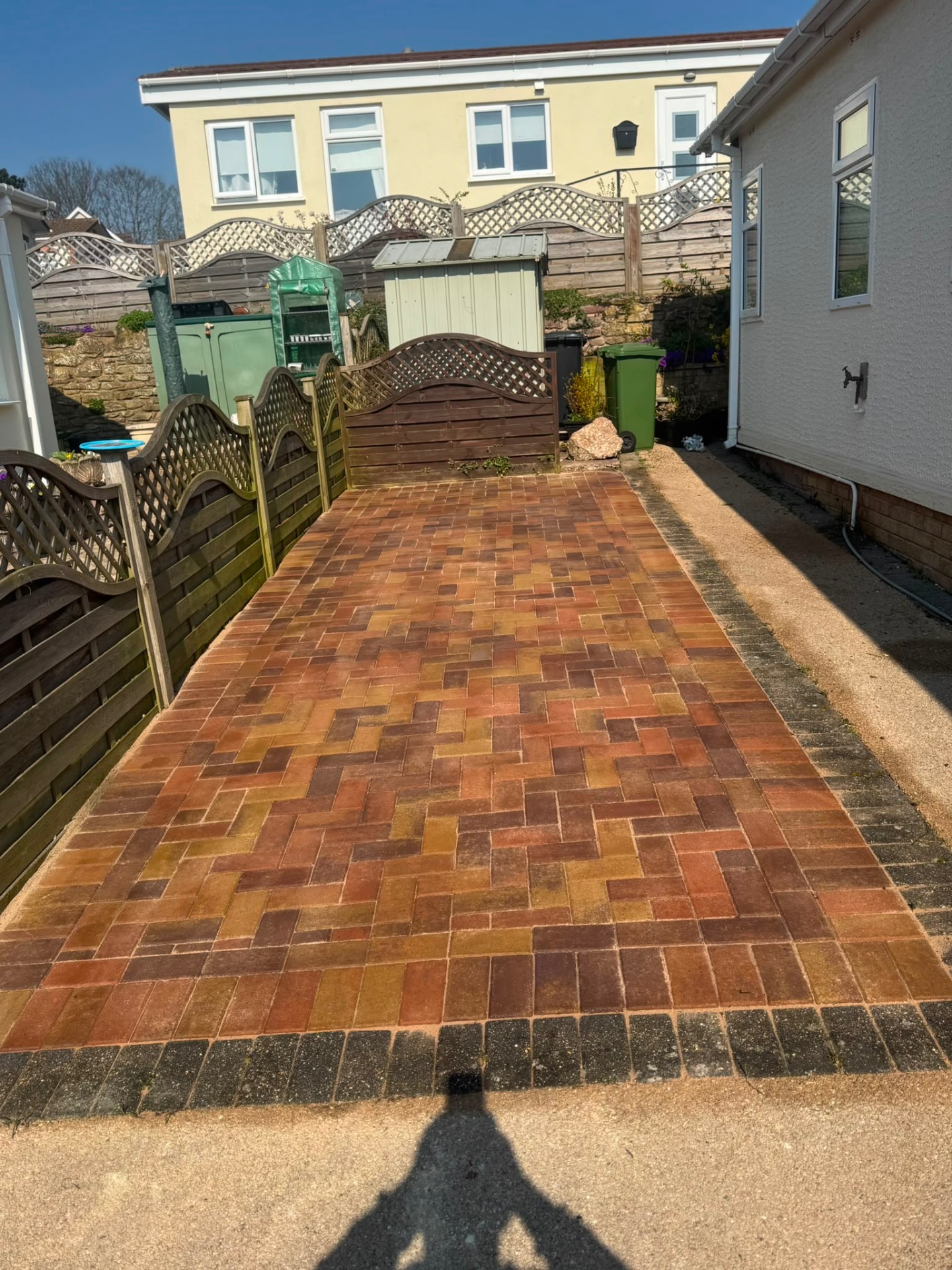 Autumn brindle block paved path running between a bungalow wall and a garden fence