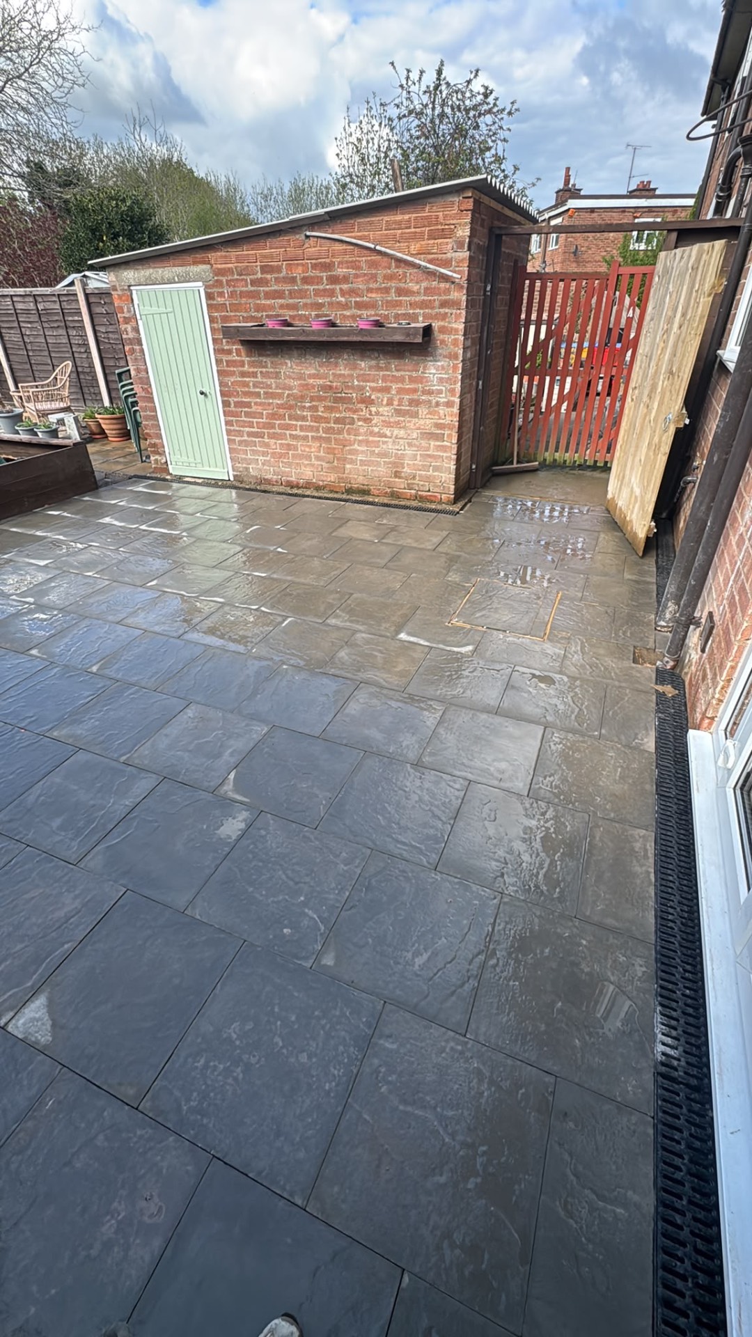 Dark grey riven patio around a brick outbuilding with a linear drainage channel in Gloucester