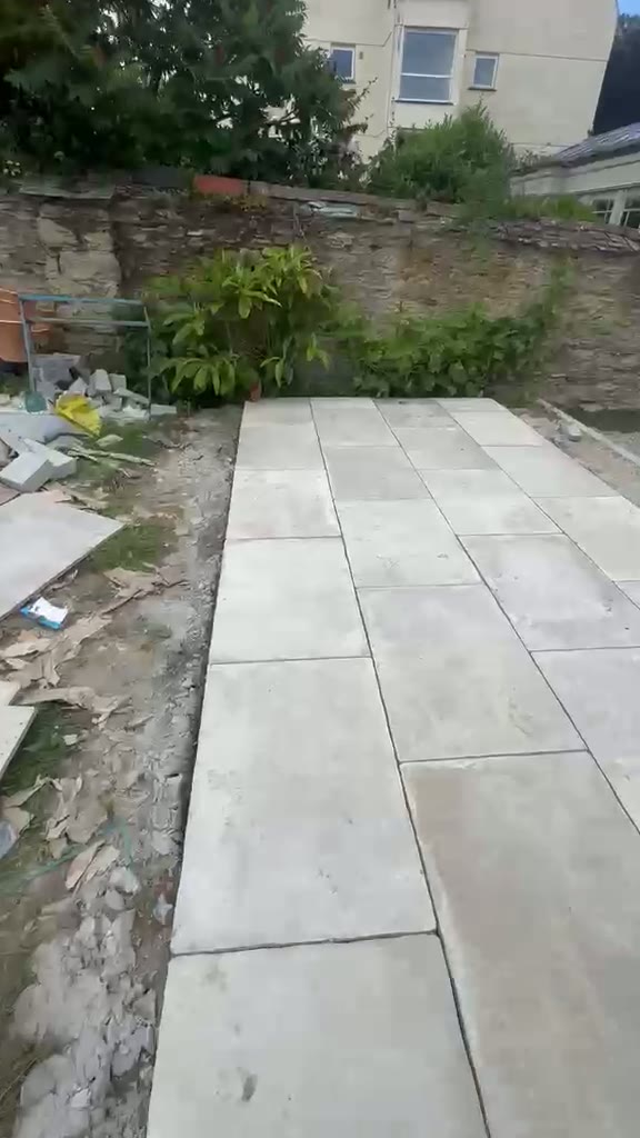 Large grey format slabs laid as a garden walkway below a stone retaining wall in Gloucester