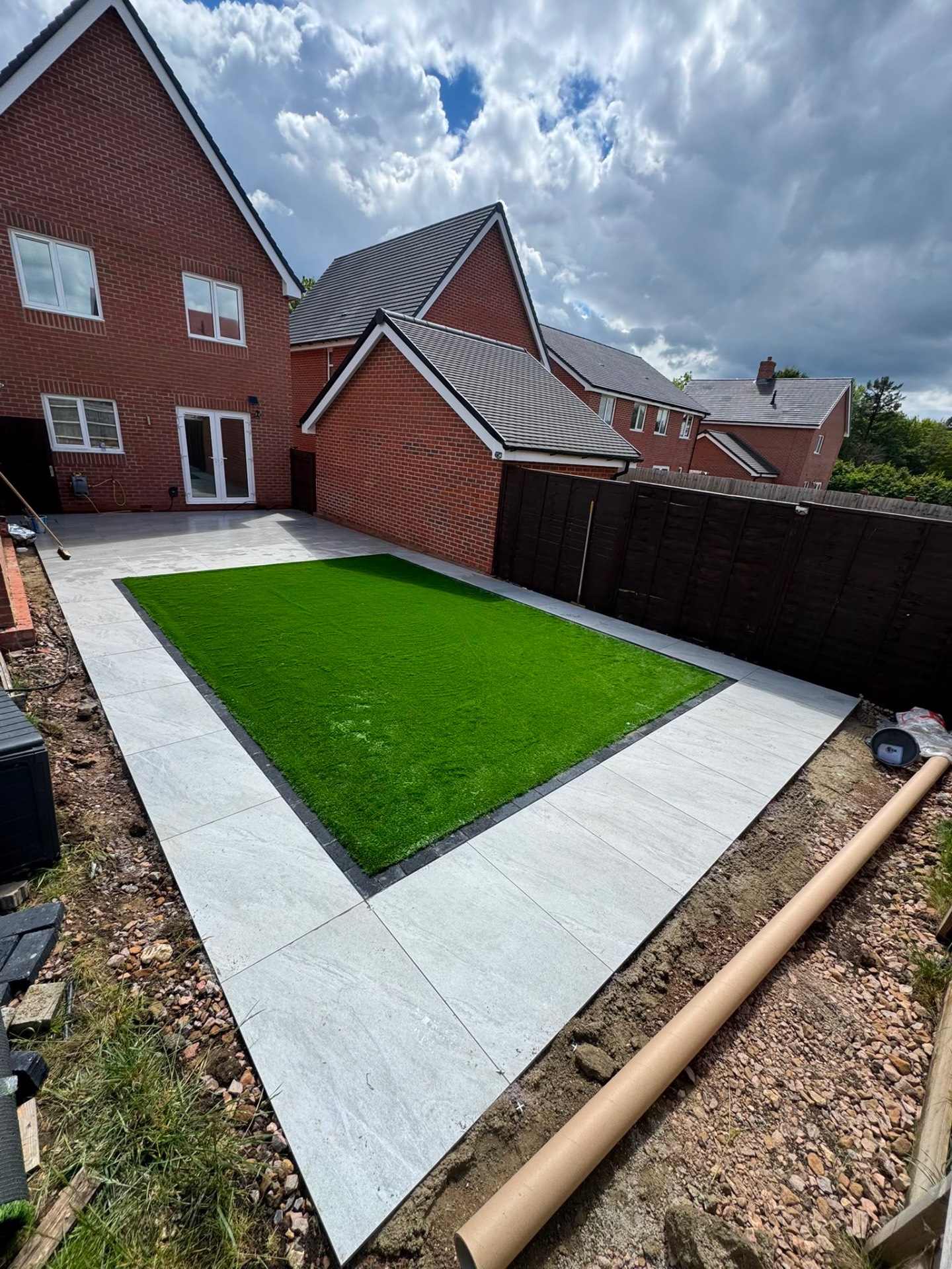 Light porcelain patio framing a rectangular lawn with charcoal sett edging in a Gloucester garden