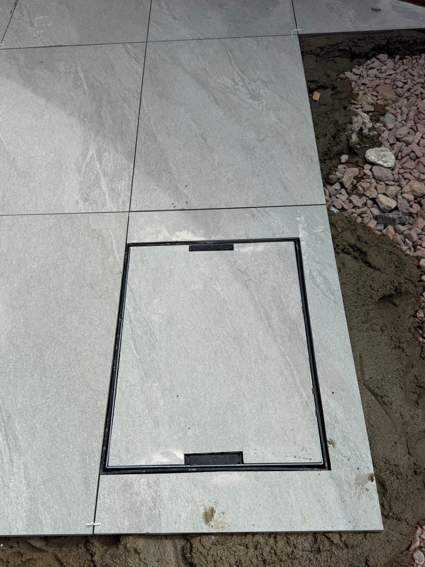 Grey porcelain slabs being laid around a recessed manhole cover during installation in Gloucester