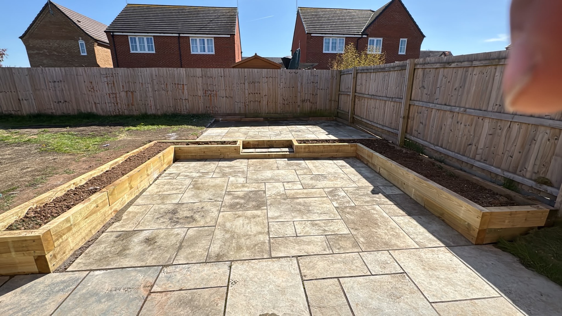 Two-tier riven slab patio with sleeper raised beds either side in a Gloucester rear garden
