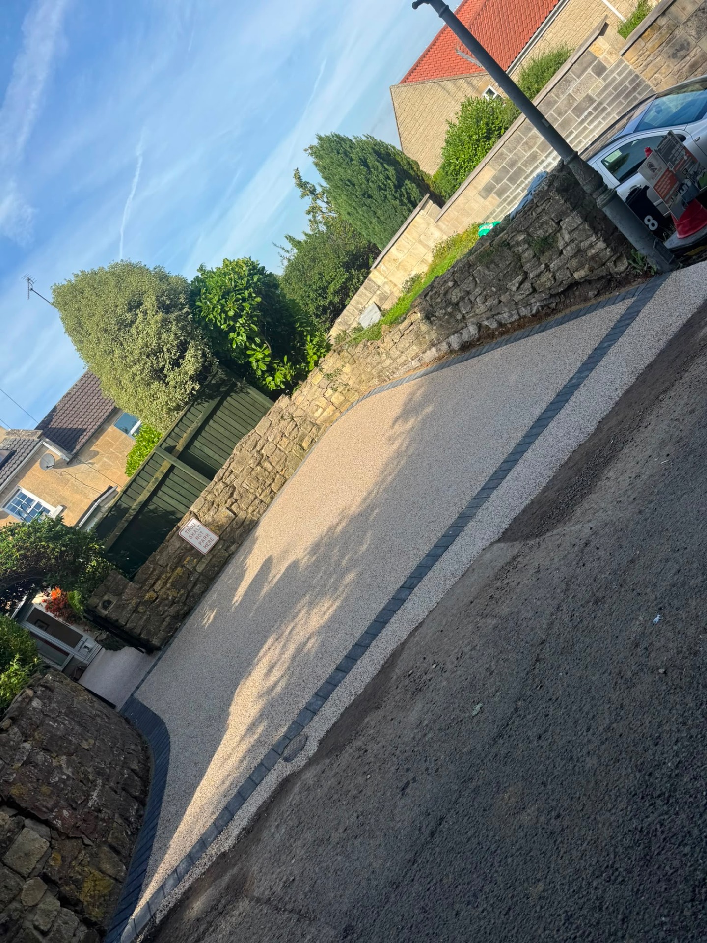 Gold resin bound driveway in Gloucester edged with dark granite setts against a stone wall