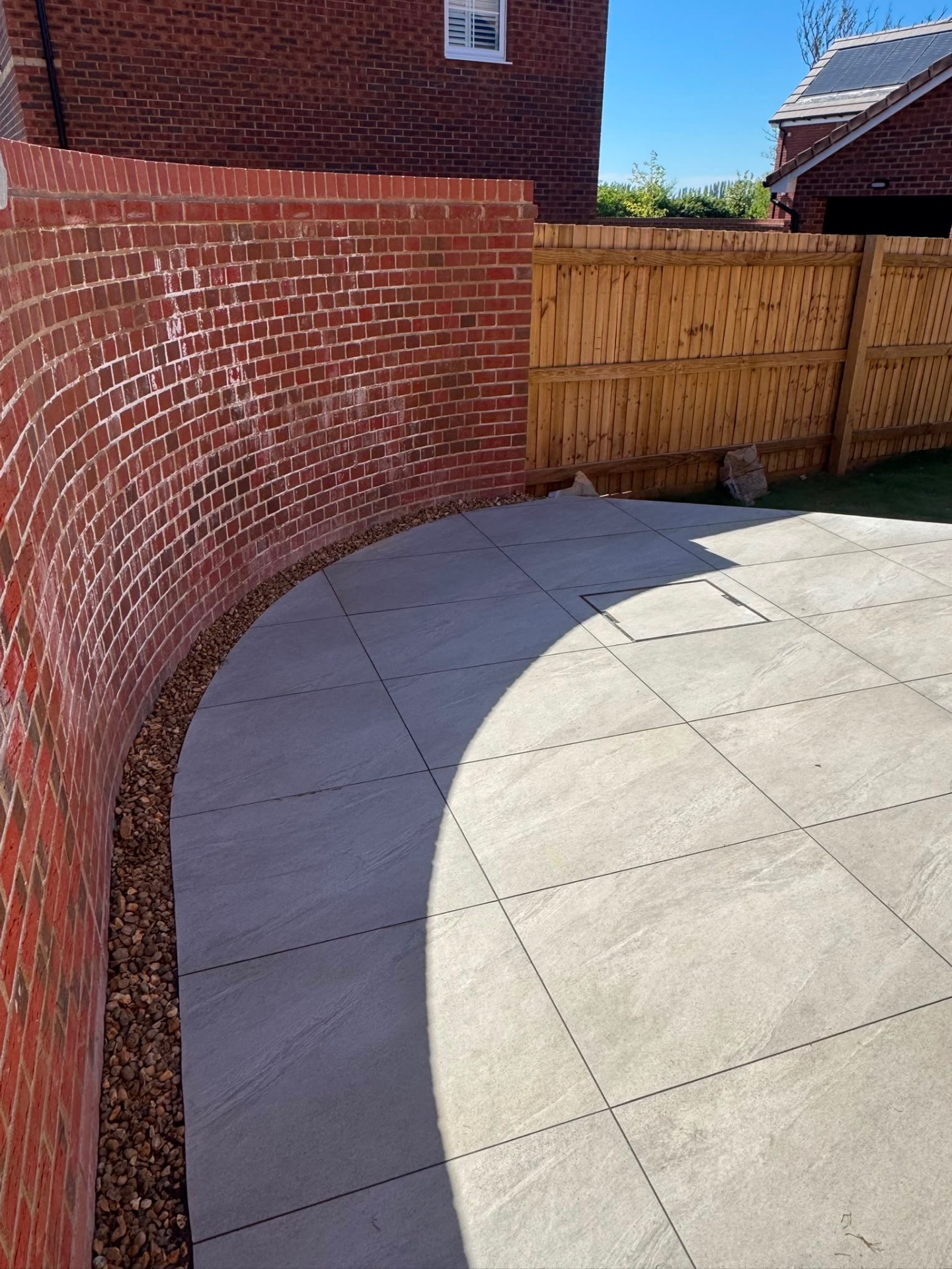 Light porcelain patio with a charcoal border curving around a red brick garden wall in Gloucester