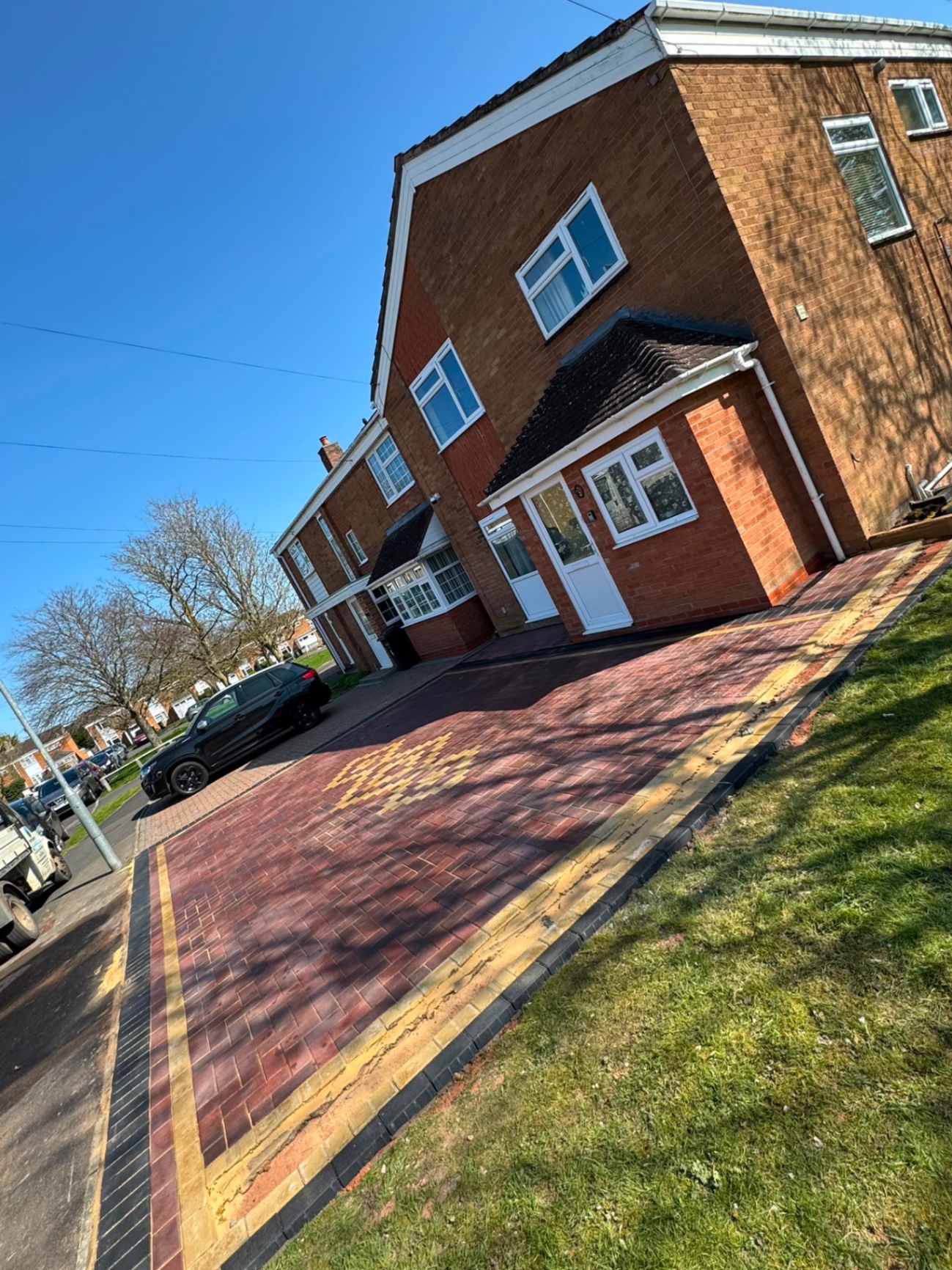 Angled view of a red brindle block driveway with twin buff borders and charcoal edging kerb in Gloucester