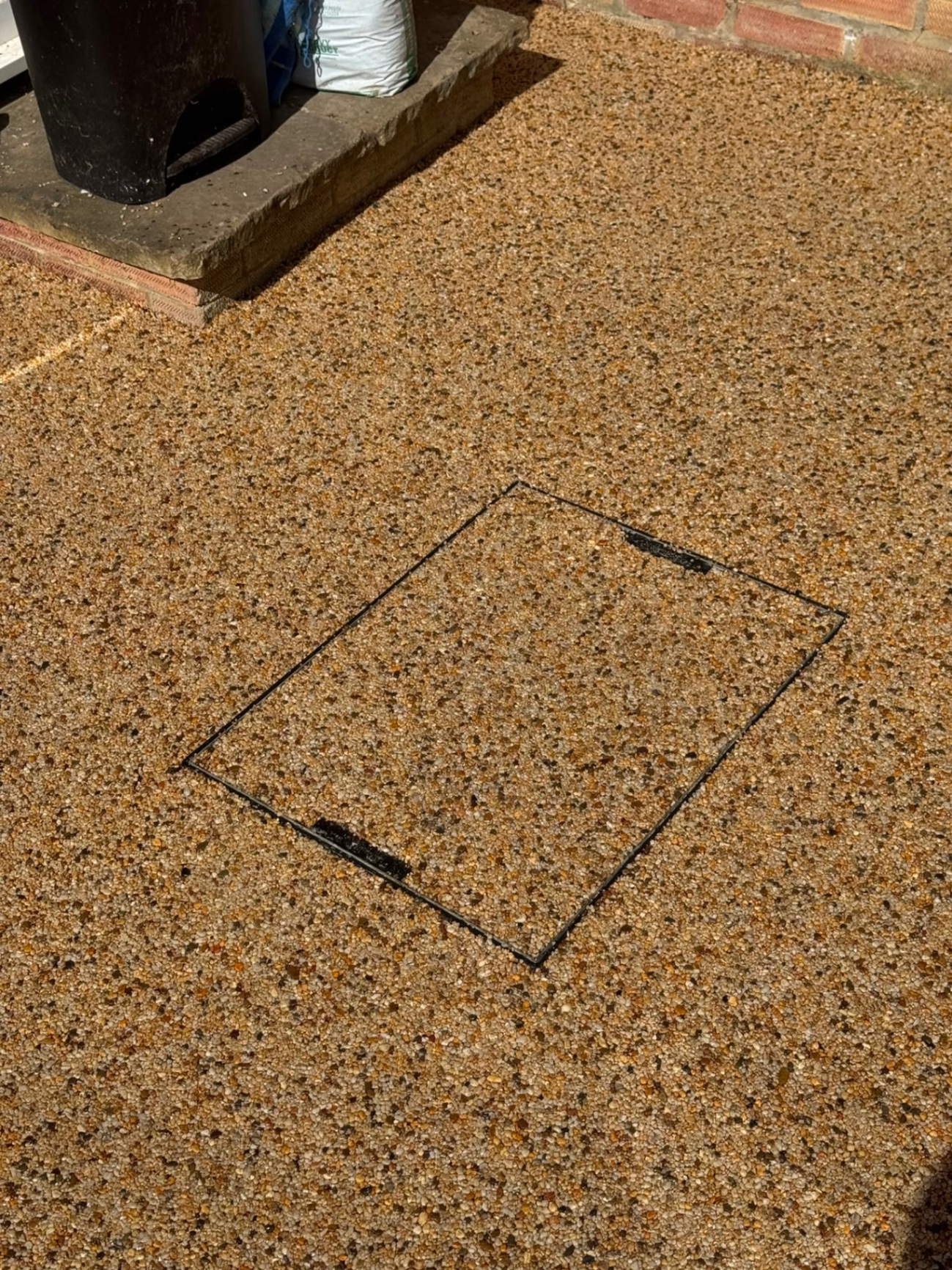Recessed manhole cover set flush into a gold resin bound surface in Gloucester