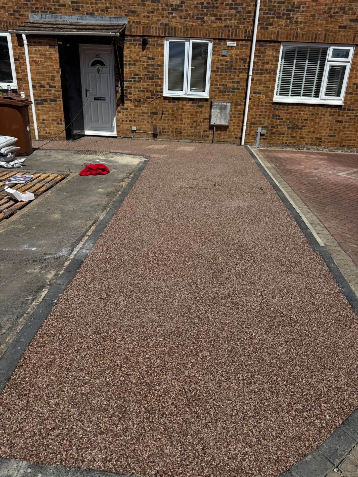 Red-brown resin bound driveway with charcoal block edging running from kerb to front door in Gloucester